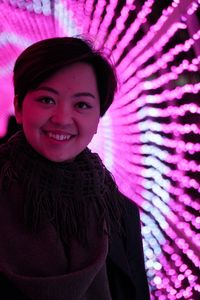 Portrait of smiling young woman against illuminated lighting equipment