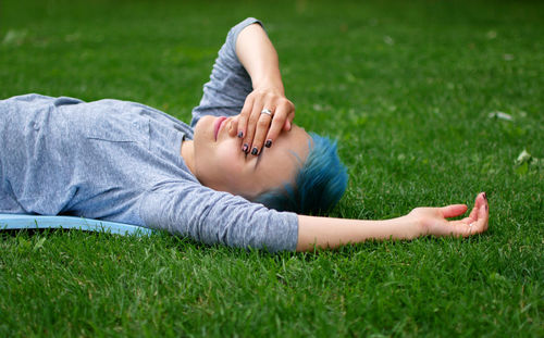 Smiling young woman covering eyes while lying on grassy field