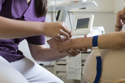 Midsection of nurse putting iv needle into patient hand at hospital