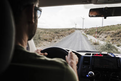 Man driving van on road passing through wind farm