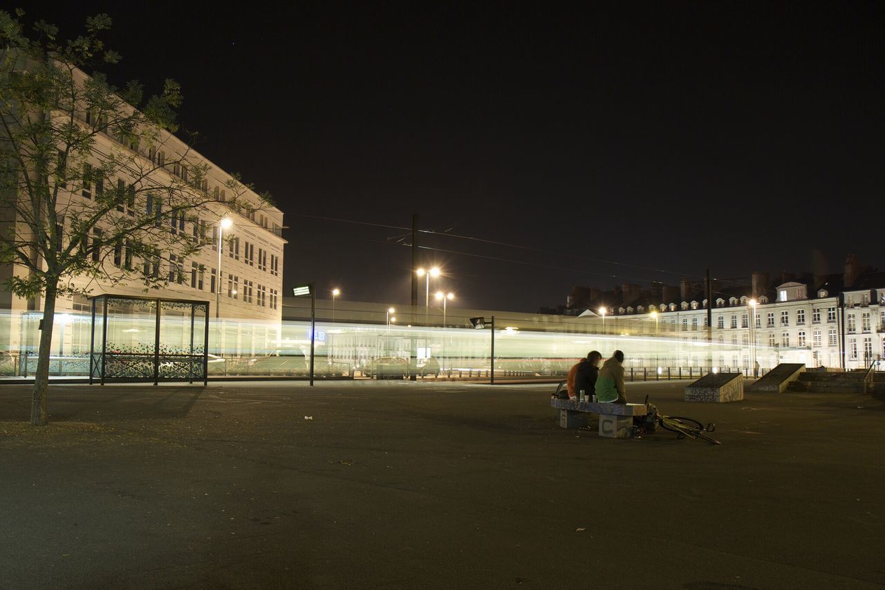 night, lifestyles, illuminated, men, leisure activity, copy space, full length, building exterior, sitting, architecture, clear sky, built structure, rear view, person, street, casual clothing, city