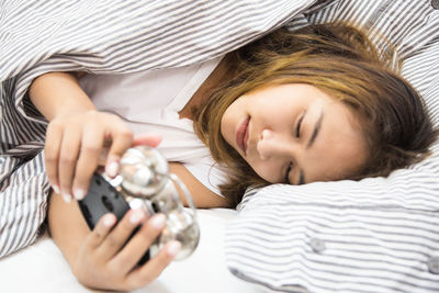 Woman holding alarm clock while lying down on bed