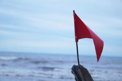 Close-up of red flag on beach against sky