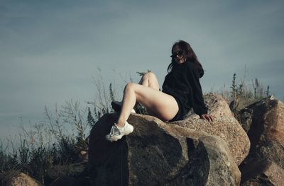 Woman sitting on rock against sky