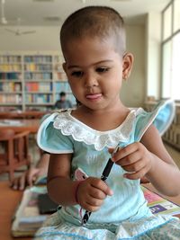 Close-up of cute girl holding pen while sitting in library