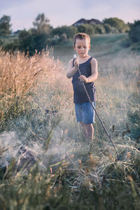 Boy holding marshmallow with stick while standing on field
