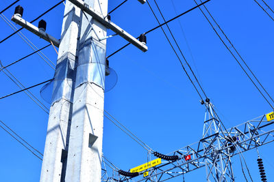 Low angle view of electricity pylon against clear blue sky