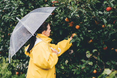 Side view of woman in raincoat with umbrella touching plants