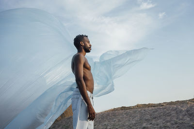 Shirtless man looking away while standing in front of foil