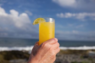 Close-up of hand holding drink at beach against sky