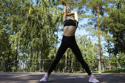 Girl in sportswear on a sunny summer day on the embankment in the park doing fitness and stretching