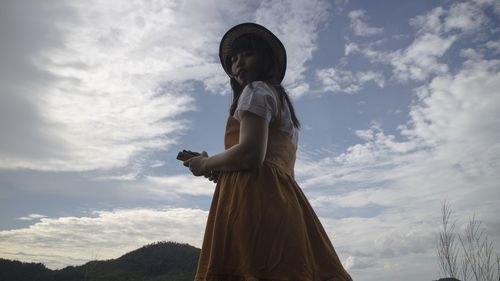 Low angle portrait of woman standing against sky