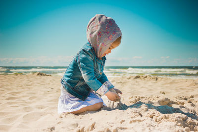 Girl playing with sand while kneeling at beach