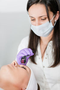 Close-up of woman lying down with while beautician using cosmetic roller on face at spa