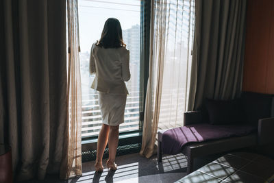 Young brunette woman business lady in white suit in hotel room on high floor