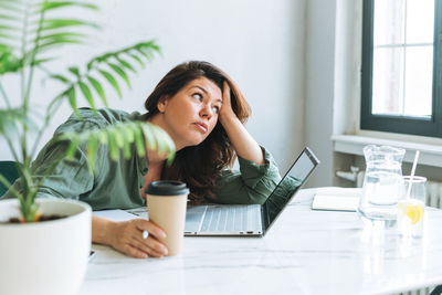 Young thinking unhappy brunette woman plus size working at laptop on table in office