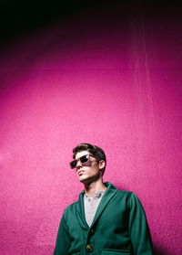 Portrait of young man wearing sunglasses standing against pink wall