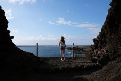 Rear view of woman standing by railing against sea