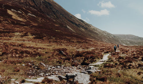 Rear view of people walking on land by mountains against sky