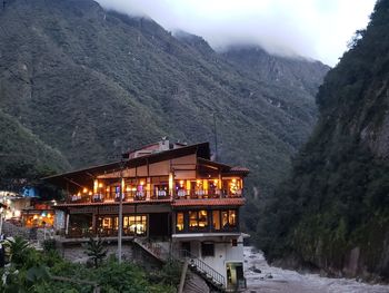 Illuminated house by buildings against mountains