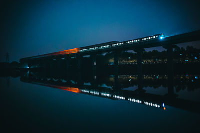 Illuminated bridge over river against sky at night