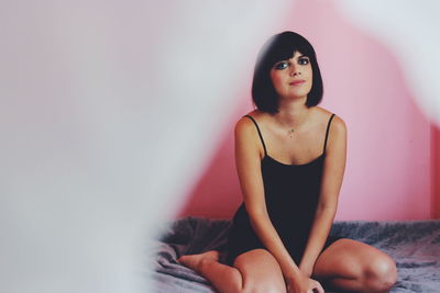 Portrait of young woman sitting against wall
