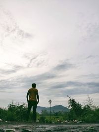 Rear view of man standing on field against sky