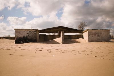 Lifeguard hut on sand at beach against cloudy sky