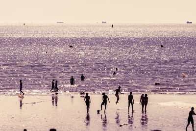 Silhouette people standing on beach against sky during sunset