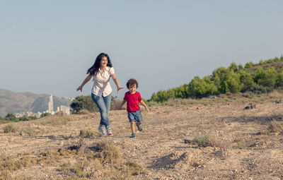 Woman with her son playing chasing him in the field far from the city