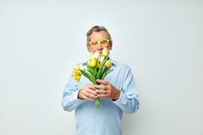 Portrait of young man holding flower against white background