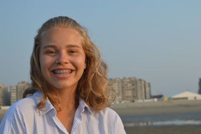 Portrait of happy teenage girl at beach against clear sky