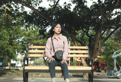 Portrait of young woman sitting on bench in park