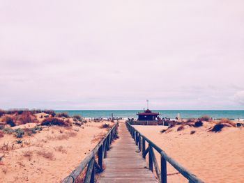 Boardwalk on beach against cloudy sky