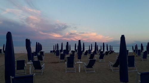 Chairs on beach against sky during sunset