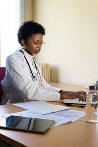 Young african american female doctor typing report on laptop while working at table in modern clinic office