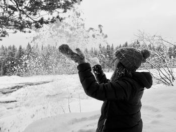 Side view of teenager girl playing with snow on field during winter