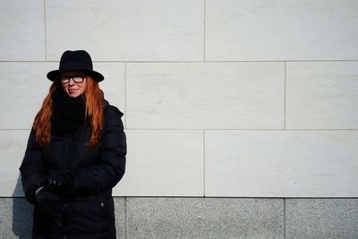 Portrait of young smiling woman standing against wall