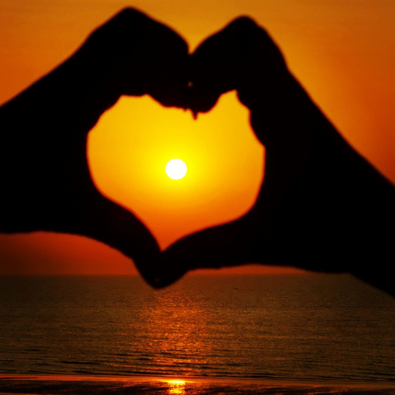 orange color, water, sunset, sky, sea, silhouette, beauty in nature, human hand, scenics - nature, nature, heart shape, sun, real people, hand, one person, tranquility, tranquil scene, love, sunlight, positive emotion, outdoors, finger