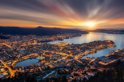 High angle view of illuminated cityscape by sea at dusk