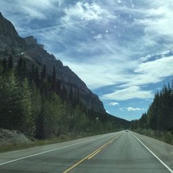 Empty road along trees and mountains against sky