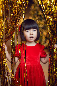 Portrait of a beautiful korean baby girl in a red dress at christmas with a gold decoration