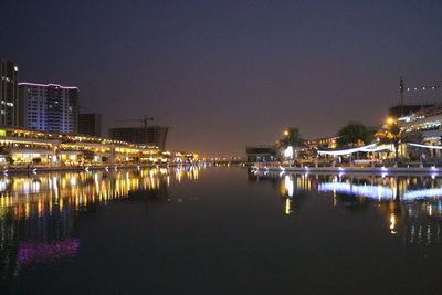 Illuminated buildings by river against sky at night