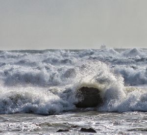 Waves splashing on shore against sky