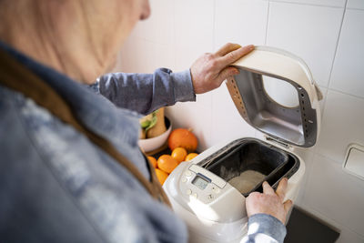 Senior man preparing bread in appliance at home