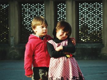 Cute siblings standing against built structure