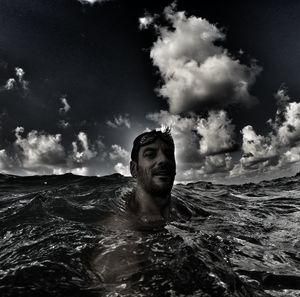 Portrait of young man swimming in sea against cloudy sky