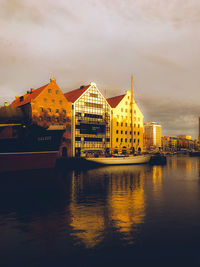 Scenic view of river by buildings against sky during sunset