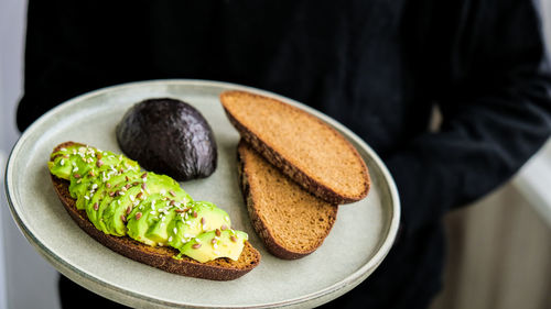 Female hand holding plate with ingredients for healthy avocado toast. ripe hass avocado, wholegrain