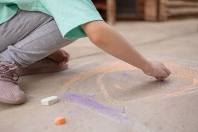 Girl draws with colorful crayons on pavement. children's drawings with chalk on wall. creative kid